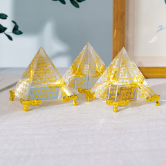 Egyptian Scripture Crystal Pyramid – three clear crystal pyramids with gold hieroglyphic engravings and golden feet arranged in a group on light linen, green foliage and wooden frame decor, collection display