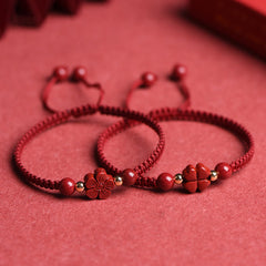 Red cord bracelet with cinnabar five-petal flower charm, gold spacer beads and polished red stone beads displayed with raw cinnabar fragments on red background