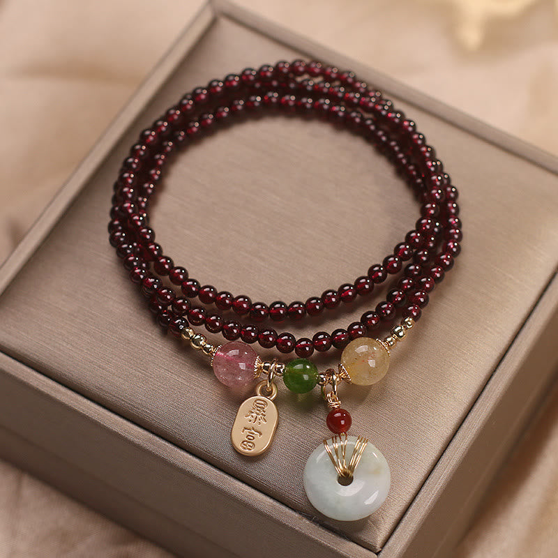 Garnet wrap bracelet with gold zhao cai wealth tag and white jade ping an kou disc in gold wire cage with mixed gemstone accent beads on champagne jewelry gift box lid