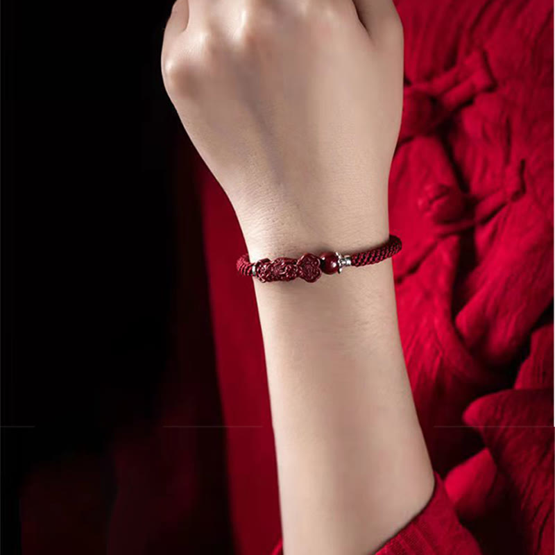 Handcrafted PiXiu Cinnabar Wealth Luck Braided Bracelet – wrist shot with red textile background, feminine style