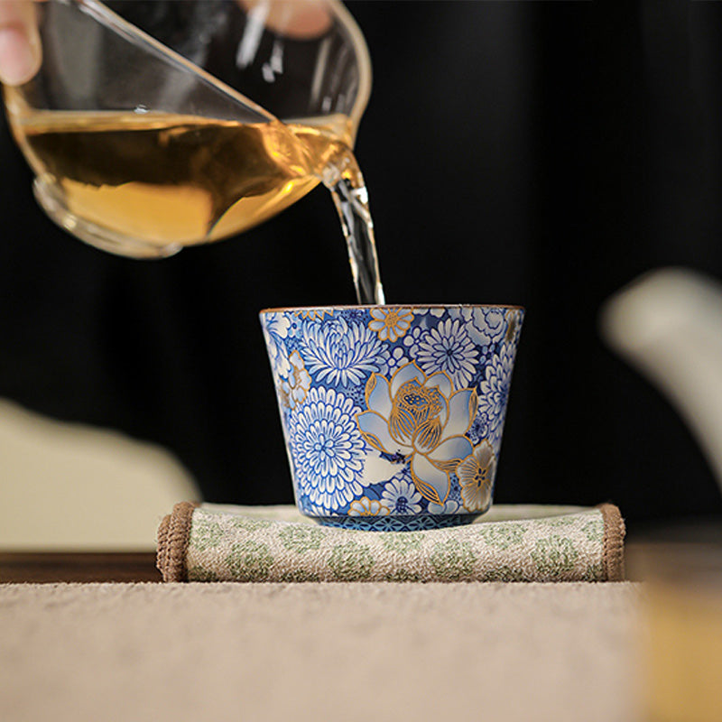 Lotus Chrysanthemum Ceramic Tea Cup - Tea streaming into blue-white cup on rolled mat, immersive
