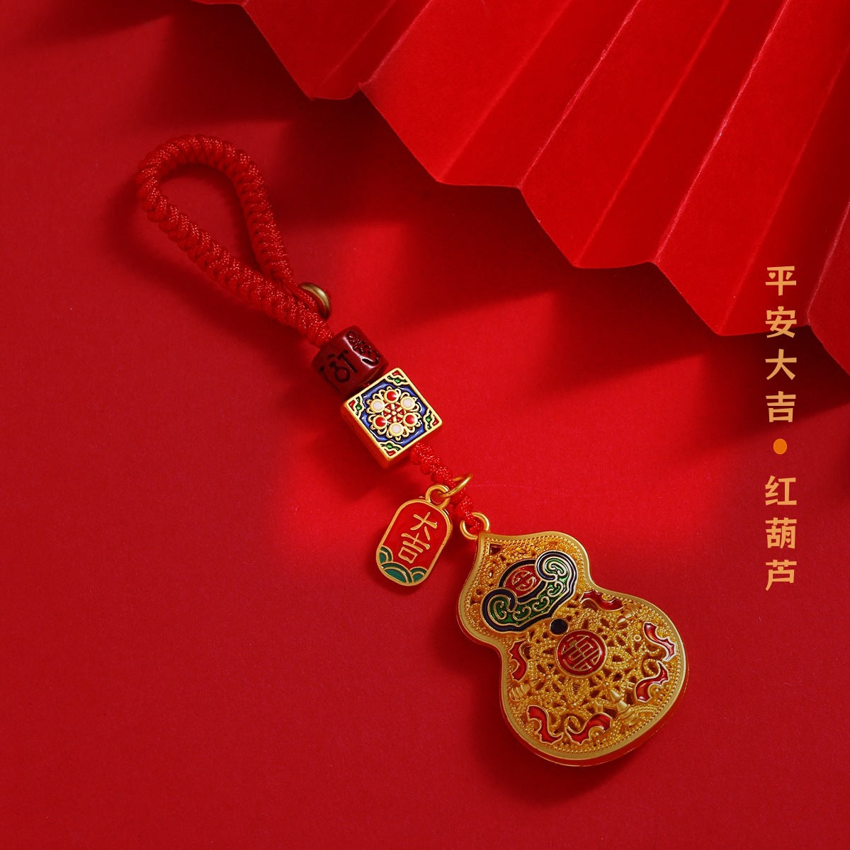 Gold enamel calabash keychain with ruyi pattern and red cord on festive red background