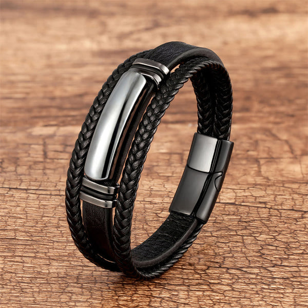 Triple-strand black leather bracelet with polished gunmetal central metal bar, braided edges, and sleek magnetic clasp on weathered wood.