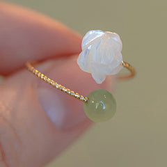 14K Gold Tridacna Jade Rose Ring – Gold twisted wire band with white shell rose and green jade bead, macro close-up on beige bokeh background