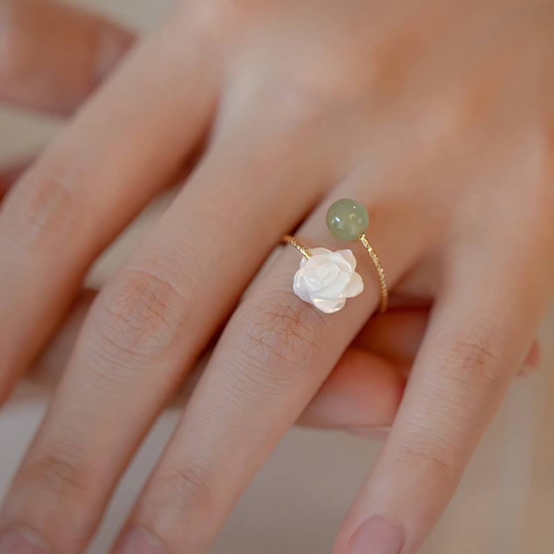 14K Gold Tridacna Jade Rose Ring – Gold ring with carved white rose and green jade bead worn on finger, soft-focus skin background, close-up side angle