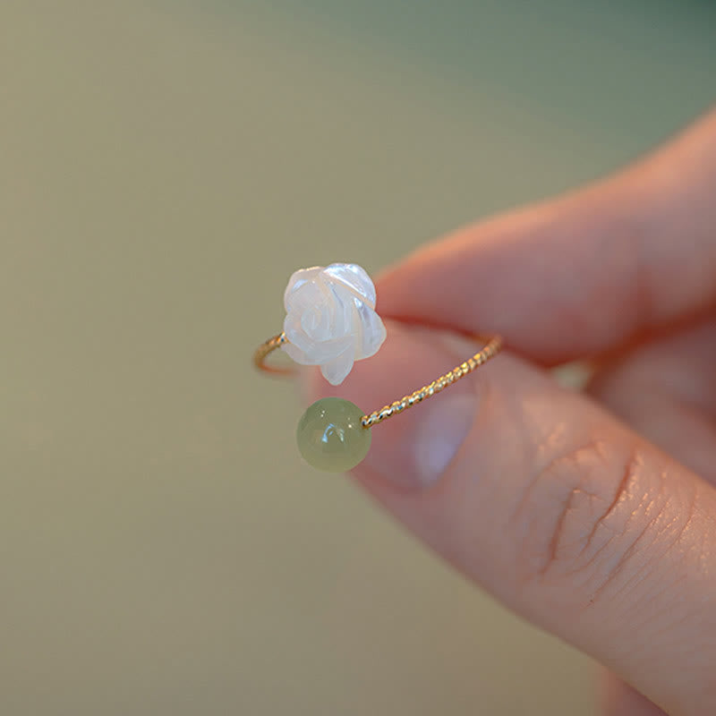 14K Gold Tridacna Jade Rose Ring – Gold open ring with shell flower and jade bead held by fingertip, soft beige bokeh, elevated side angle