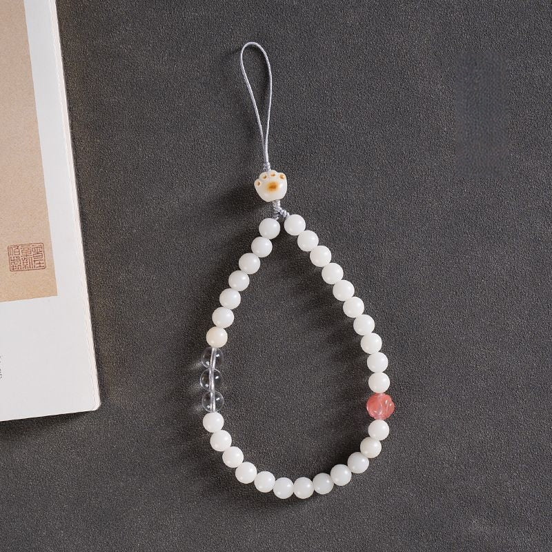 White Jade Bodhi & Jadeite Crystal Phone Charm – White round bodhi beads with pink crystal accent and carved cat charm on gray surface