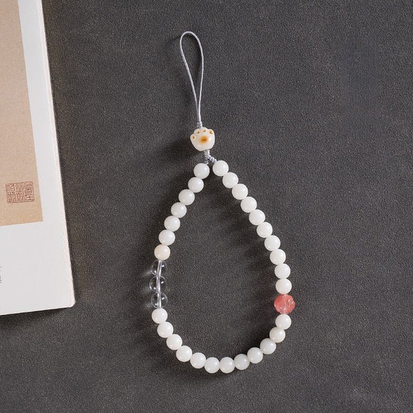 White Jade Bodhi & Jadeite Crystal Phone Charm – White round bodhi beads with pink crystal accent and carved cat charm on gray surface