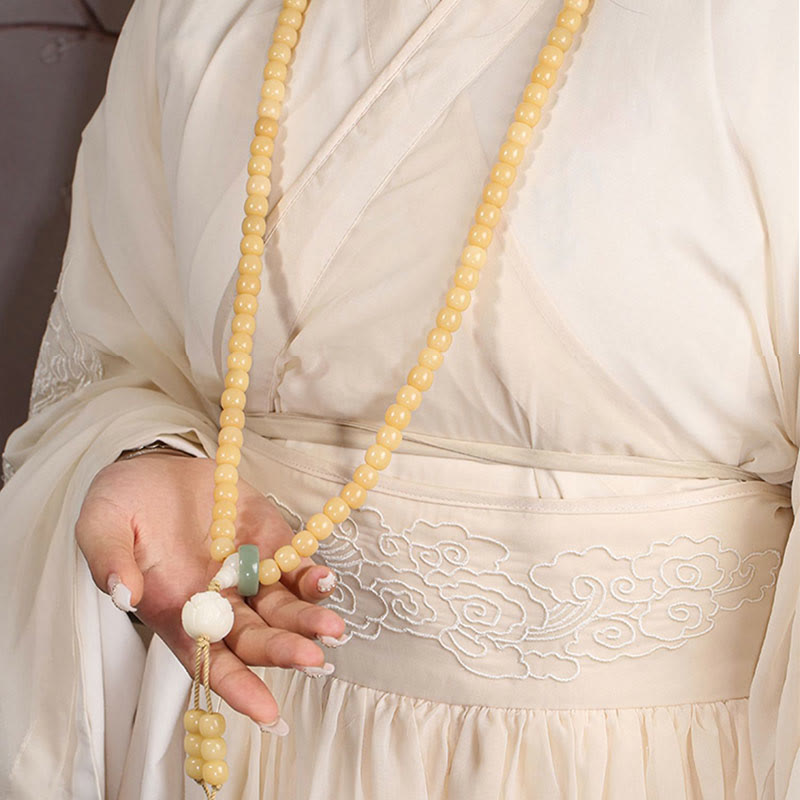 Bodhi Seed Lotus Dzi Bracelet - Hand holding bodhi mala strand with lotus tassel against gray backdrop, dzi bead