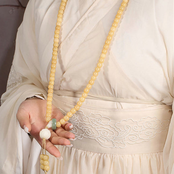 Bodhi Seed Lotus Dzi Bracelet - Hand holding bodhi mala strand with lotus tassel against gray backdrop, dzi bead