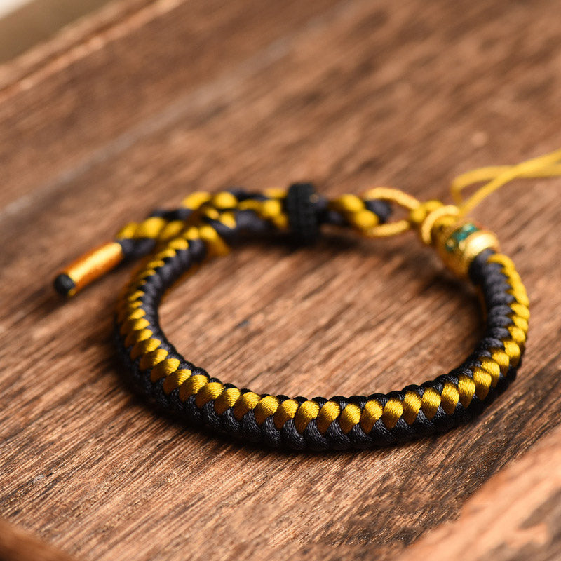 Tibetan Black Gold Dragon Scale Bracelet – diagonal view on dark wood grain, intricate braid texture, spiritual jewelry