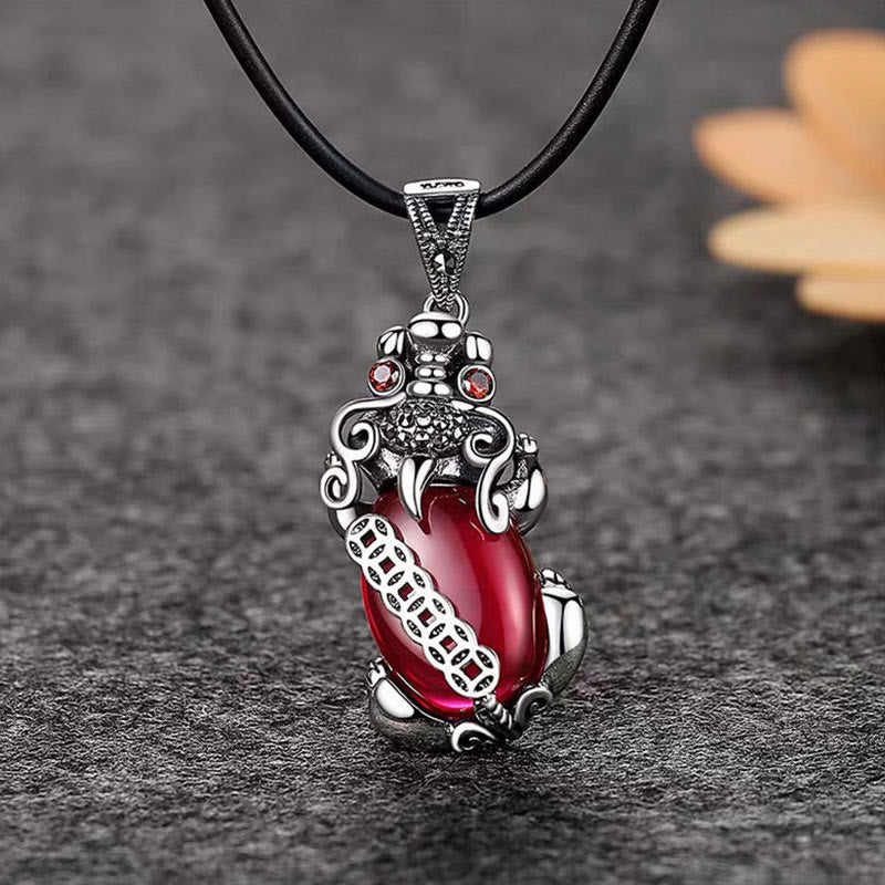 Garnet PiXiu Necklace – PiXiu with garnet on black cord over dark textured surface with leaf accent, protection