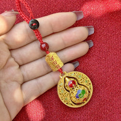 Hand holding gold rotating calabash disc keychain with peace talisman and red cord