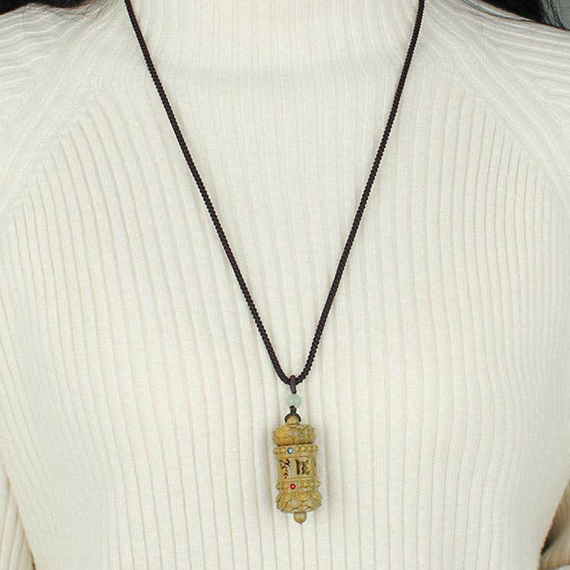 Om Mani Padme Hum Necklace – Gold prayer wheel pendant with stone accents on dark cord, worn on white ribbed sweater