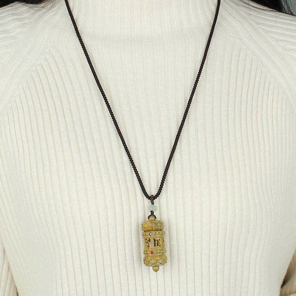 Om Mani Padme Hum Necklace – Gold prayer wheel pendant with stone accents on dark cord, worn on white ribbed sweater