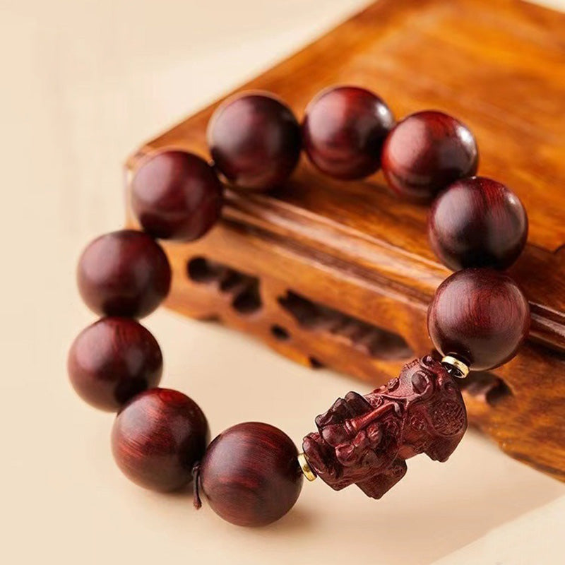 Red Sandalwood PiXiu Bracelet – Rich red sandalwood beads draped on carved wooden stand, warm tone bracelet