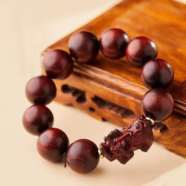 Red Sandalwood PiXiu Bracelet – Rich red sandalwood beads draped on carved wooden stand, warm tone bracelet
