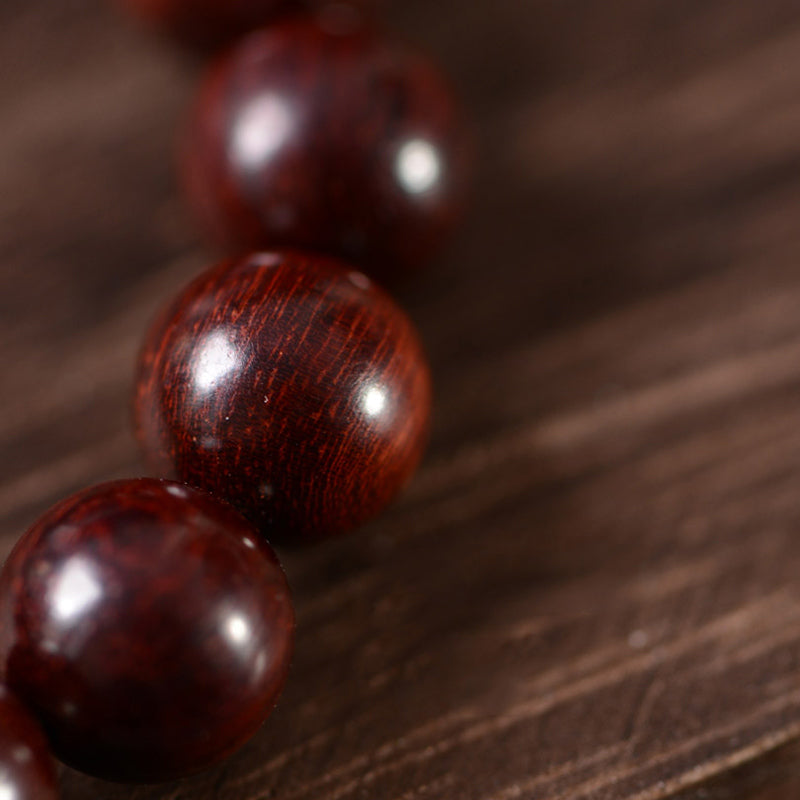 Red Sandalwood Om Bracelet – macro of glossy red sandalwood beads on matching wood surface, fine wood grain visible