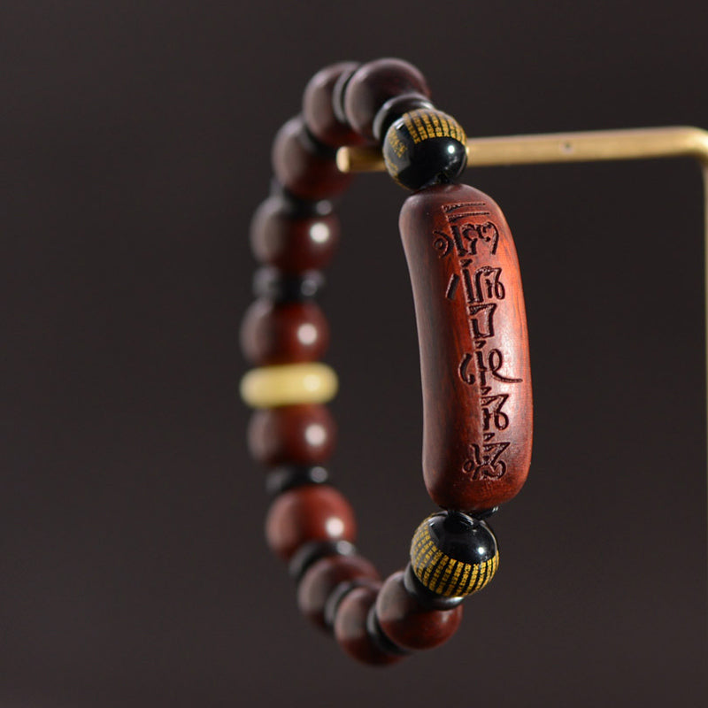 Red Sandalwood Om Bracelet – suspended view on dark background, wood beads with gold-patterned accents, mala bead bracelet