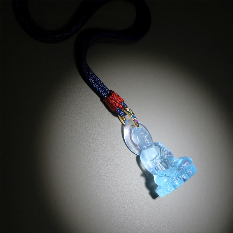 Blue Tathagata Medicine Buddha Liuli Crystal Necklace – pale aquamarine pendant with gold multi-stone bail and braided navy cord, red knot fastener, light gray surface