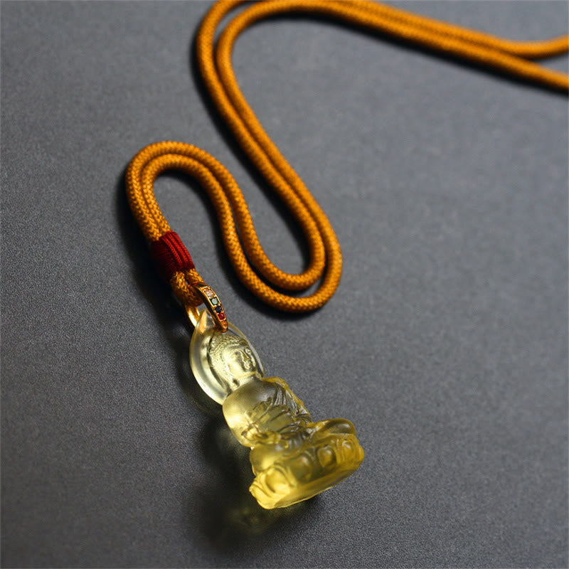 Blue Tathagata Medicine Buddha Liuli Crystal Necklace – warm amber Buddha in meditation on mustard braided cord, red knot and green gem accent, dark gray studio