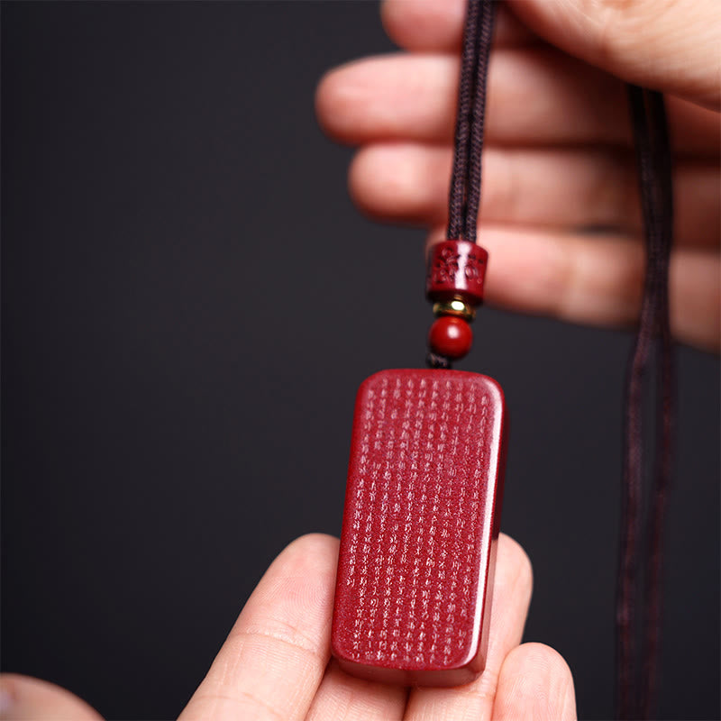 Heart Sutra Cinnabar Amulet – fingers holding pendant to showcase micro-carved scripture text, red talisman