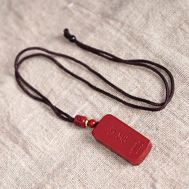Cinnabar Lotus Pendant – angled view on natural fabric showing adjustable cord knot and red bead accents