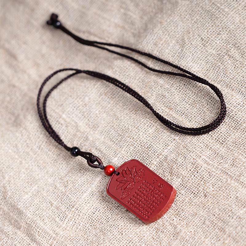 Lotus Cinnabar Necklace – top-down flat lay on linen fabric showing lotus carving and sutra engraving, zen jewelry
