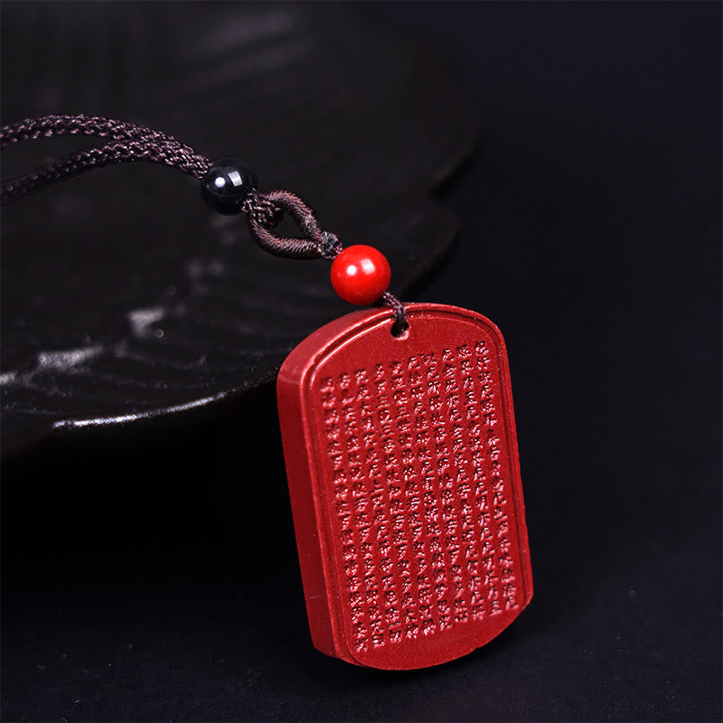 Cinnabar Sutra Pendant – three-quarter view on dark surface with black and red accent beads, carved amulet