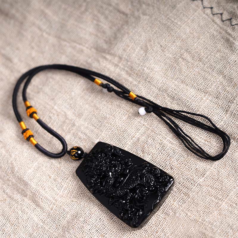 Black Obsidian Dragon Carved Pendant – Linen flat lay with orange accent knots and adjustable closure, wearable