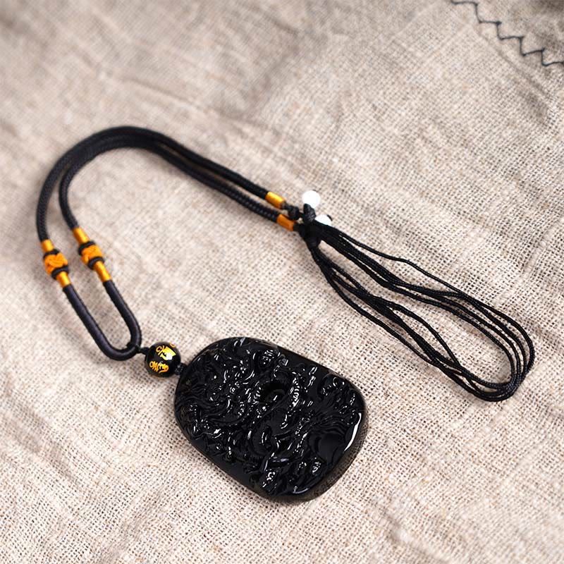 Black Obsidian Dragon Carved Pendant – Flat lay on linen with adjustable cord and amber accent knots, artisanal