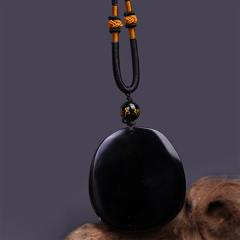 Black Obsidian Round Dragon Pendant – dragon disc flat-laid with amber and white beads on linen, grounded