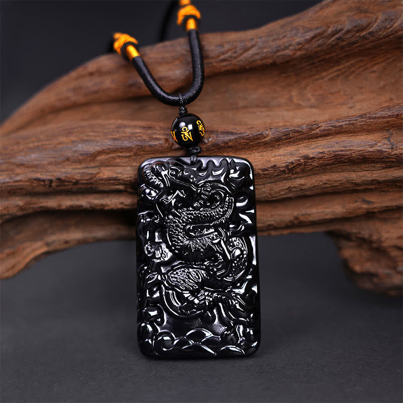 Black Obsidian Dragon Pendant – full dragon body coiled on braided cord with mantra bead on driftwood, auspicious