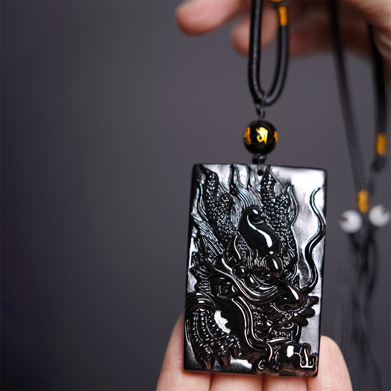 Black Obsidian Dragon Pendant – close-up dragon head relief held between fingers on gray, fierce