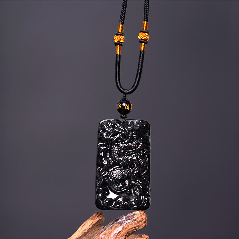 Black Obsidian Dragon Pendant – front view with gold knot cord and inscribed bead on driftwood, confident