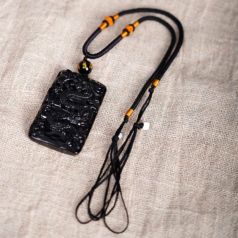 Black Obsidian Dragon Pendant – coiled dragon with cord tassels and amber beads on linen, artisan