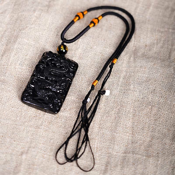 Black Obsidian Dragon Pendant – coiled dragon with cord tassels and amber beads on linen, artisan