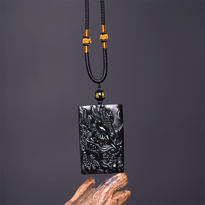 Black Obsidian Dragon Pendant – dragon plaque with gold knots and mantra bead on dark gray, bold