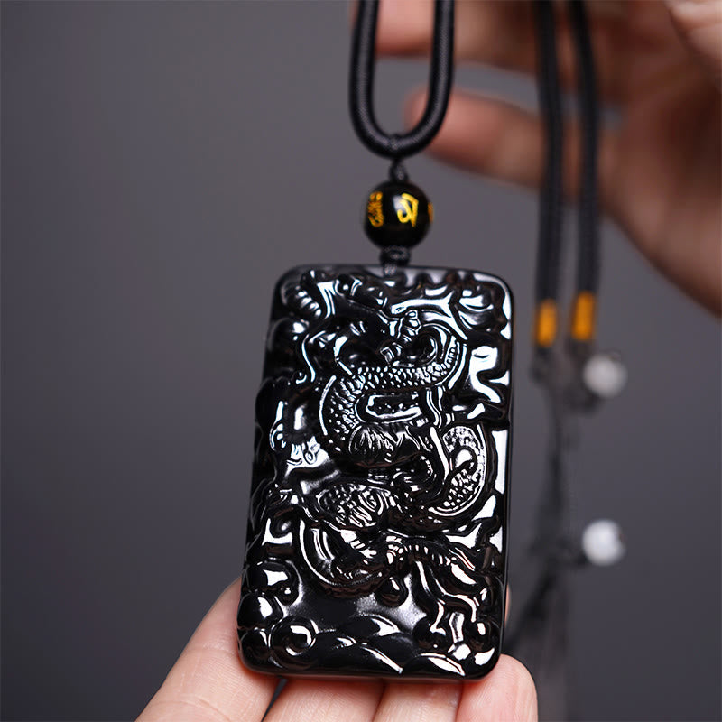 Black Obsidian Dragon Pendant – rectangular carved dragon plaque held in hand on dark gray, powerful
