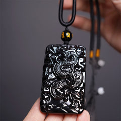 Black Obsidian Dragon Pendant – rectangular carved dragon plaque held in hand on dark gray, powerful