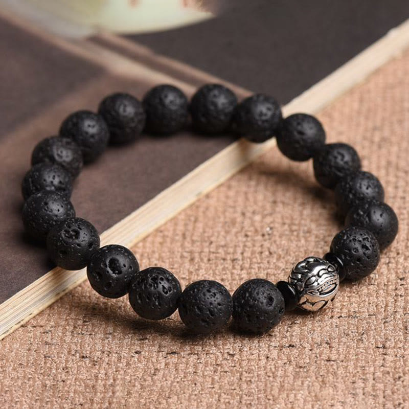 Lava Stone PiXiu Bracelet on natural fiber textile, open book background, volcanic rock bead, mindful jewelry