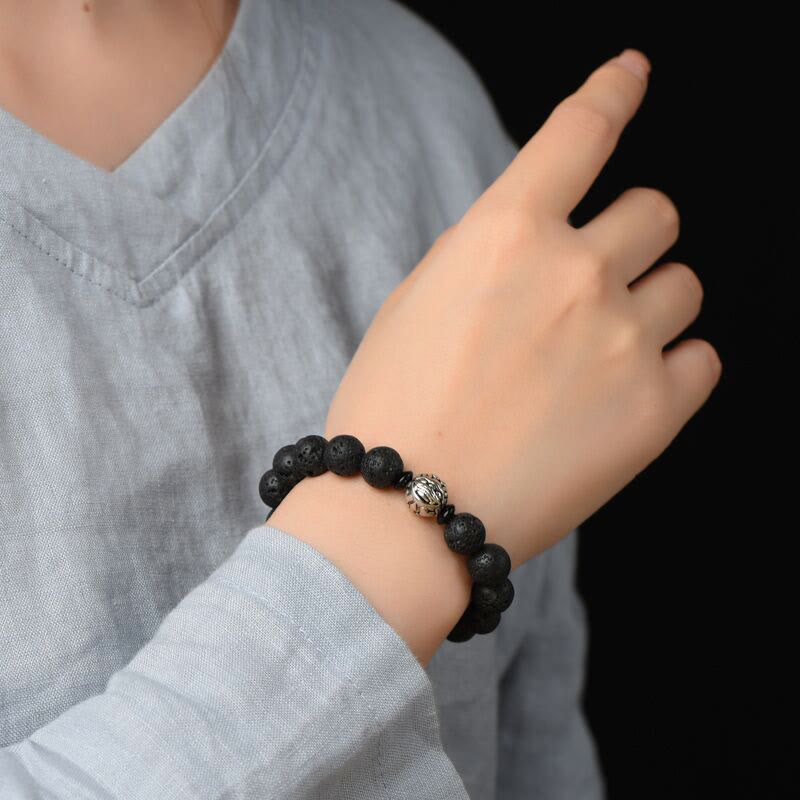 Black Lava Rock PiXiu Wealth Bracelet on gray sleeve, black background, porous stone texture, men's bracelet