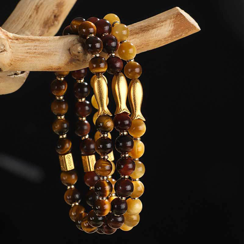 Tiger Eye Koi Fish Courage Bracelet – three bracelets on driftwood against black, gold fish charms, prosperity