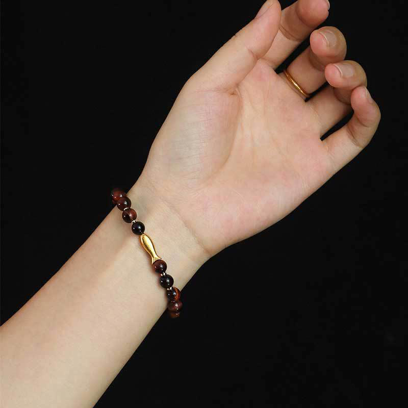 Tiger Eye Koi Fish Courage Bracelet – red tiger eye with gold fish charm on wrist against black background