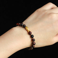 Tiger Eye Koi Fish Courage Bracelet – burgundy tiger eye beads with gold fish charm on wrist, black bg close-up