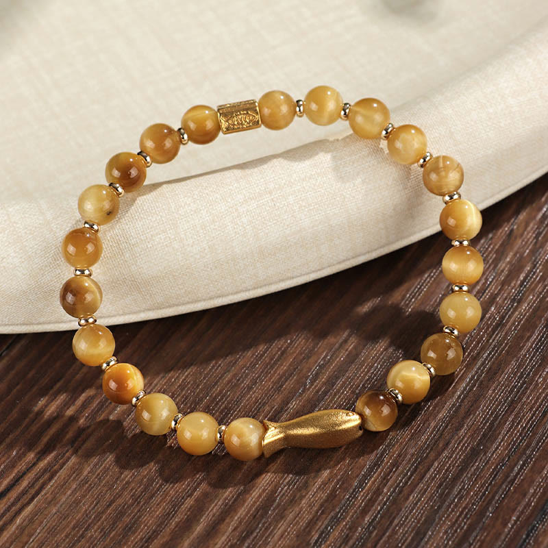 Tiger Eye Koi Fish Courage Bracelet – golden tiger eye with gold fish charm on dark wood surface, 45-degree view