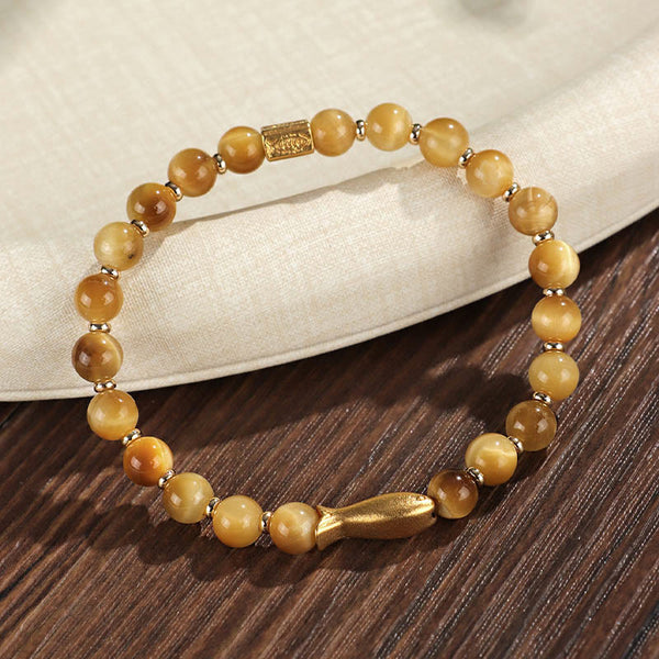 Tiger Eye Koi Fish Courage Bracelet – golden tiger eye with gold fish charm on dark wood surface, 45-degree view