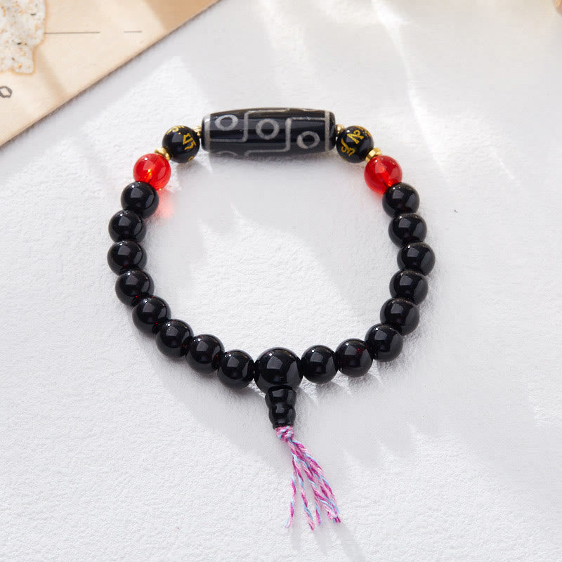 Tibetan Nine-Eye Dzi Bead Black Onyx Bracelet – flat lay on white fabric, circular loop with colored tassel, dzi bead