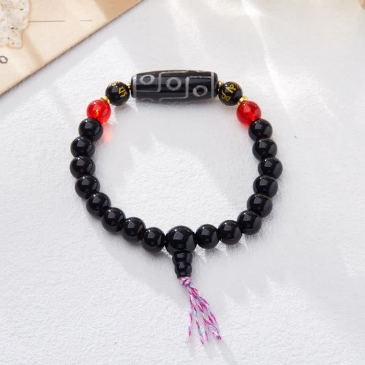 Tibetan Nine-Eye Dzi Bead Black Onyx Bracelet – flat lay on white fabric, circular loop with colored tassel, dzi bead