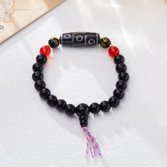 Tibetan Nine-Eye Dzi Bead Black Onyx Bracelet – flat lay on white fabric, circular loop with colored tassel, dzi bead